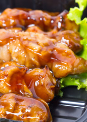 Chicken teriyaki with skewers inblack tray.