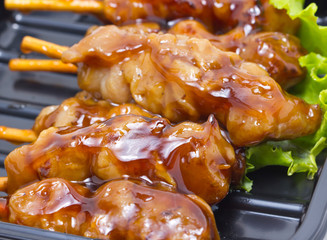 Chicken teriyaki with skewers inblack tray.