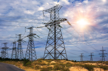 High-voltage power lines and stormy sky with the sun