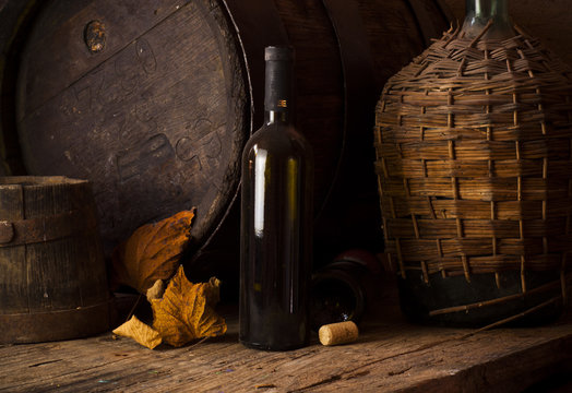 Still life with wine bottles, glasses and oak barrels.