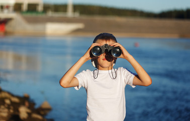 Happy child looking in nautical binoculars  against blue water background. Kid having fun on nature. Summer sea dream and imagination.