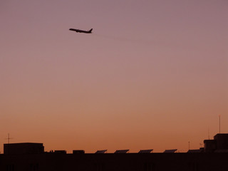 Airplane takeoff at dusk against red skies and rooftop silhouette in Mallorca, Spain.