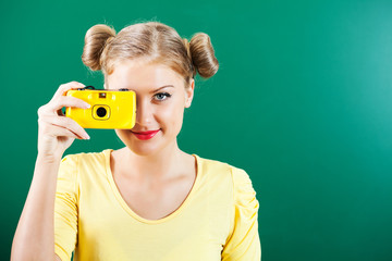 Happy student girl holding photo camera in front of blackboard