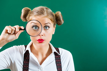 Student girl with loupe in front of blackboard