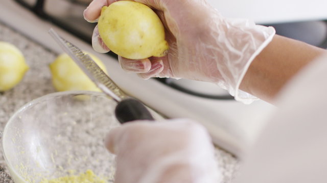 4K Over the shoulder view of a lemon being used on a zester to remove the rind, in slow motion