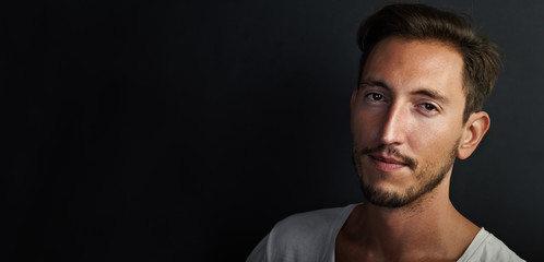 Portrait of handsome young man wearing white tshirt on the black background . Wide