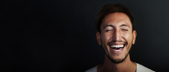 Portrait of cute young man wearing white tshirt and laughing  a lot. Wide