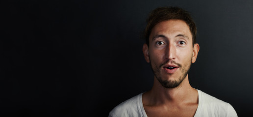 Portrait of young man wearing white tshirt and looks surprised. Wide