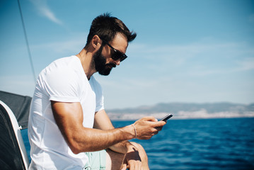 Photo of bearded man looking in his smartphone on the boat