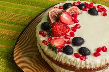 Nude cake with strawberries, figs, grapes and pomegranates on big brown plate. Plate is on green tablecloth with stripes. 