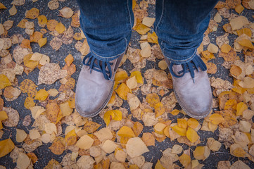 Conceptual image of legs in boots on the autumn leaves. Feet shoes walking in nature