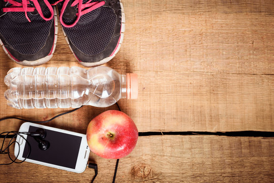 Sport equipment. Sneakers, water, apple, smartphone and earphones on wooden background. Clothes for running. 