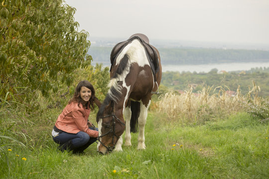 Young girl stroking domestic horse, grazing grass.