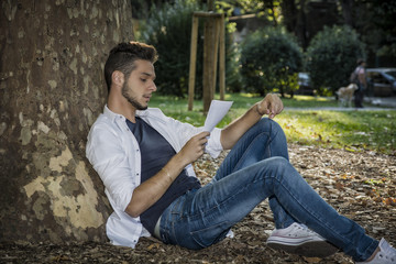 Young Man Reading Paper Sheets Relaxing at Park
