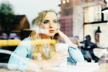 Beautiful young woman drinking coffee at cafe and looking throug