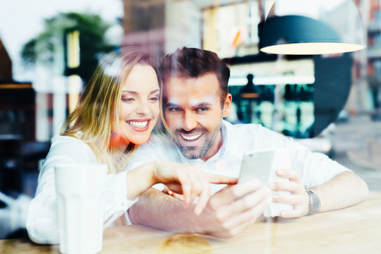 Photo of a happy couple looking at smartphone at cafe