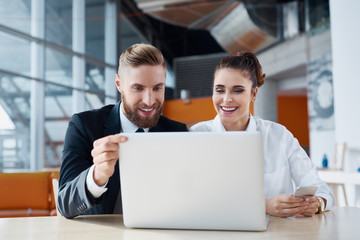 Two happy business people working on laptop at office