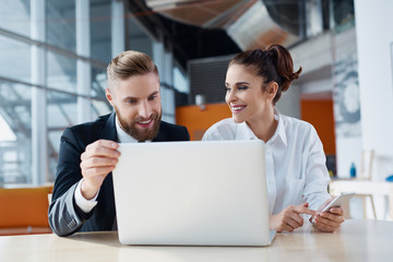 Two cheerful business people working with laptop at office