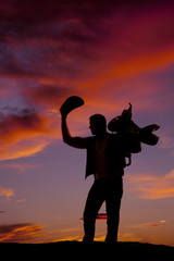 Fototapeta na wymiar silhouette of a cowboy holding his hat up and a saddle on should