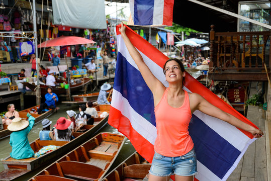 Joyful woman having fun at Damnoen Saduak floating market showing Thailand flag at Bangkok. Female tourist on Asia Travel.