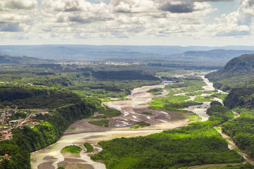 Aerial shot of the lush Amazon rainforest in Ecuador, with towering trees and a mountain in the background. The vast basin stretches out below.