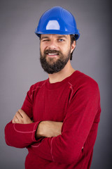 Happy young worker with hardhat and arms folded blinking