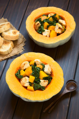 Pumpkin and chard salad with croutons served in pumpkin halves, photographed on dark wood with natural light (Selective Focus, Focus on the lower half of the first salad)