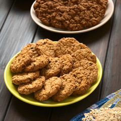 Oatmeal and apple cookies on plate with chocolate oatmeal cookies in the back, photographed with natural light (Selective Focus, Focus on the front of the cookies in the middle)
