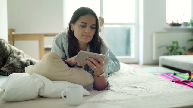 Woman lying on the bed and typing message on smartphone
