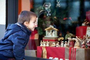 Fototapeta na wymiar Sweet little boy, looking through a window in shop, decorated fo
