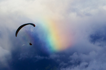 Experience the exhilaration of paragliding against a picturesque cloudy sky and vibrant natural rainbow,showcasing the irresistible allure of colors.