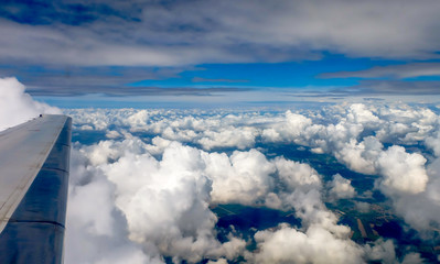 Fototapeta na wymiar Aerial view through an aircraft window, clouds and blue sky,with partial view of the aircraft's wing