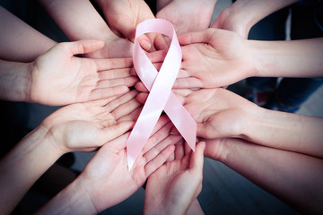 Group of female hands with pink ribbon as breast cancer awareness symbol, closeup