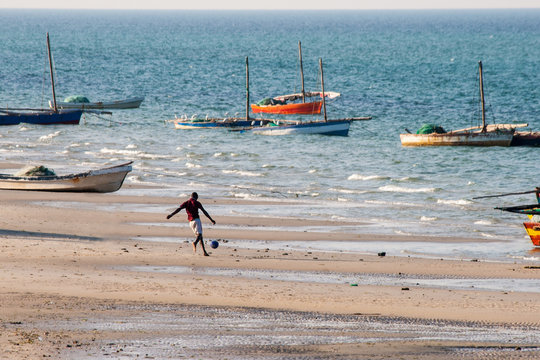 Man plays soccer and in the background sailing boats are anchored at the beach of Vilanculos.