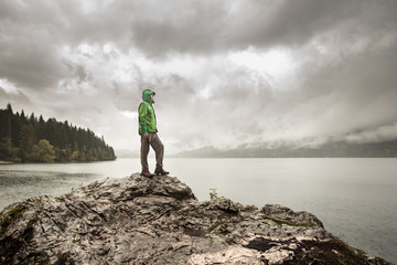 Man standing on a rock beside a mountain lake in rain