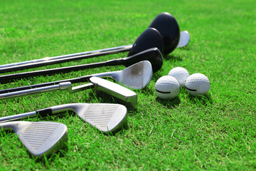 Different golf clubs in a row and balls on a green grass