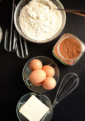 Black table with butter, cocoa, eggs and white flour
