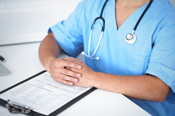 Portrait of unknown male surgeon doctor sitting at the table in hospital office, stethoscope