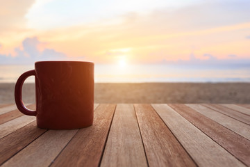 Coffee cup on wood table at sunset or sunrise beach