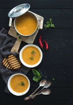 Red lentil soup with spices, herbs, bread in a rustic metal saucepan and bowls, over dark wood backdrop, top view