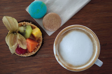 Cup of hot coffee and fruit tart and colorful magaron on table