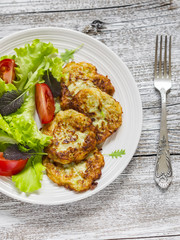 zucchini pancake and fresh vegetable salad on white plate on bright wooden surface