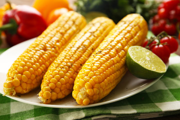 Appetizing grilled corn served with vegetables and green plaid pattern napkin