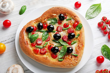 Fresh tasty heart shaped pizza decorated with vegetables and herbs on wooden background
