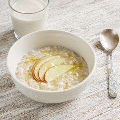 porridge with apple and honey in a white bowl and a glass of  natural yoghurt on white wooden table