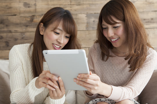Two young women looking at a tablet on the sofa