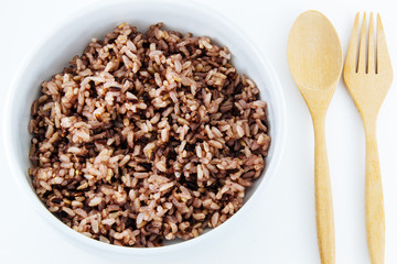 Black rice in bowl and wooden spoon on white background.