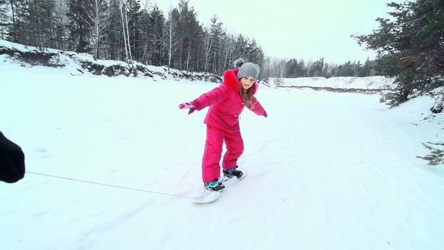 Little girl balancing on a snowskate pulled on a leash 