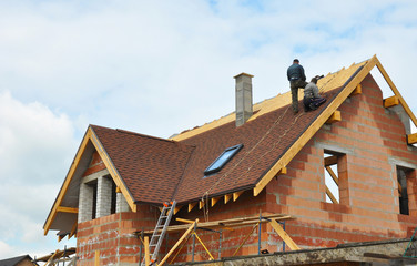 Roofing Construction and Building New Brick House with Modular Chimney, Skylights, Attic, Dormers and Eaves Exterior. Roofers Install, Repair Asphalt Shingles or Bitumen Tiles on the Rooftop Outdoor