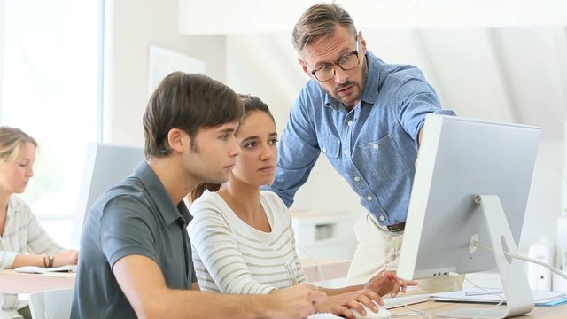 Teacher with group of students in class working on desktop